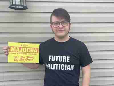 Photo of Elijah Majocha holding a sign that announces his run for school board